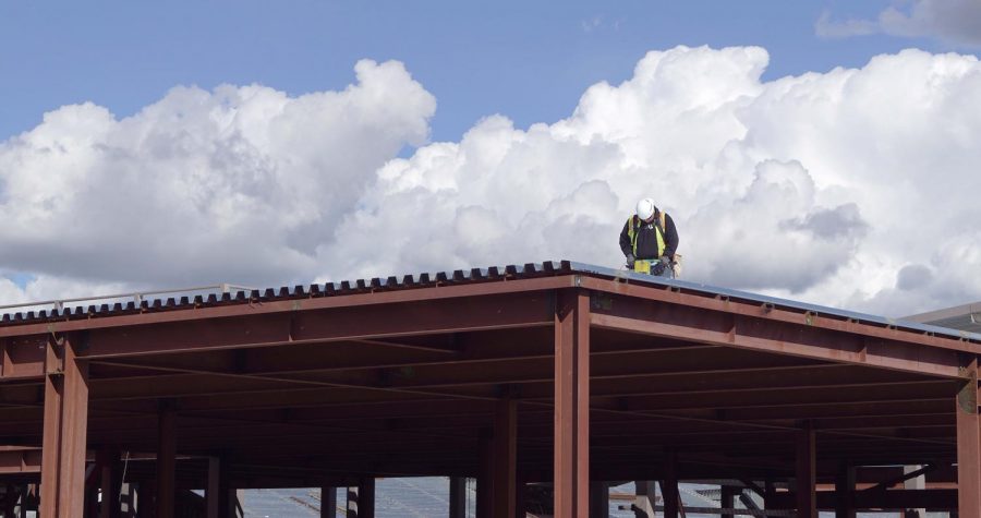 A construction worker stands atop the roof of the new campus building as he works on the framework of the building. 