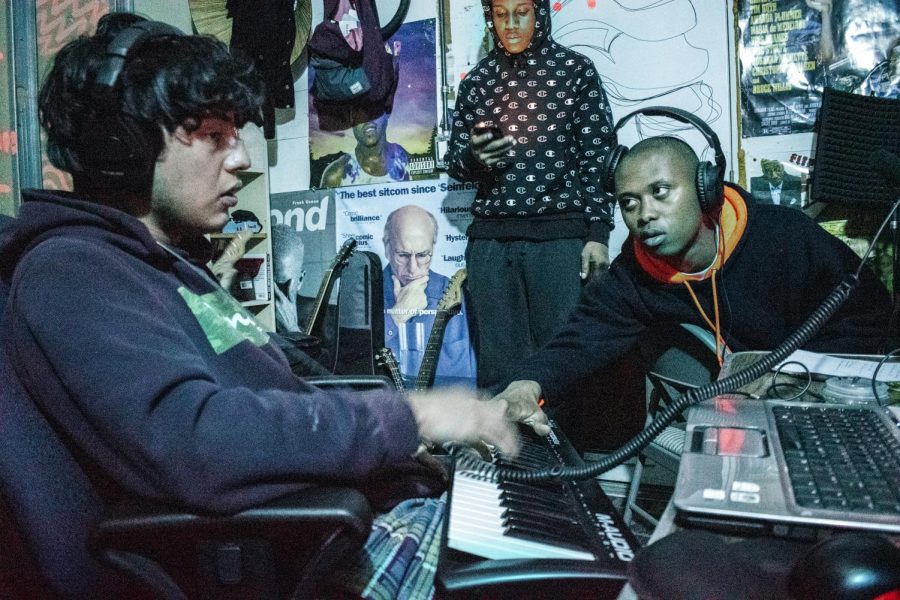 Above, AG Club crafts a song in their garage studio. Seated left is Loui, who uses a digital keyboard to mix together the instrumental. Seated right, reaching over, is Babyboy, who asks Loui how certain affects can be added to make his vocals more interesting. Behind them is Jody Fontaine, mulling over lyrics he wrote.