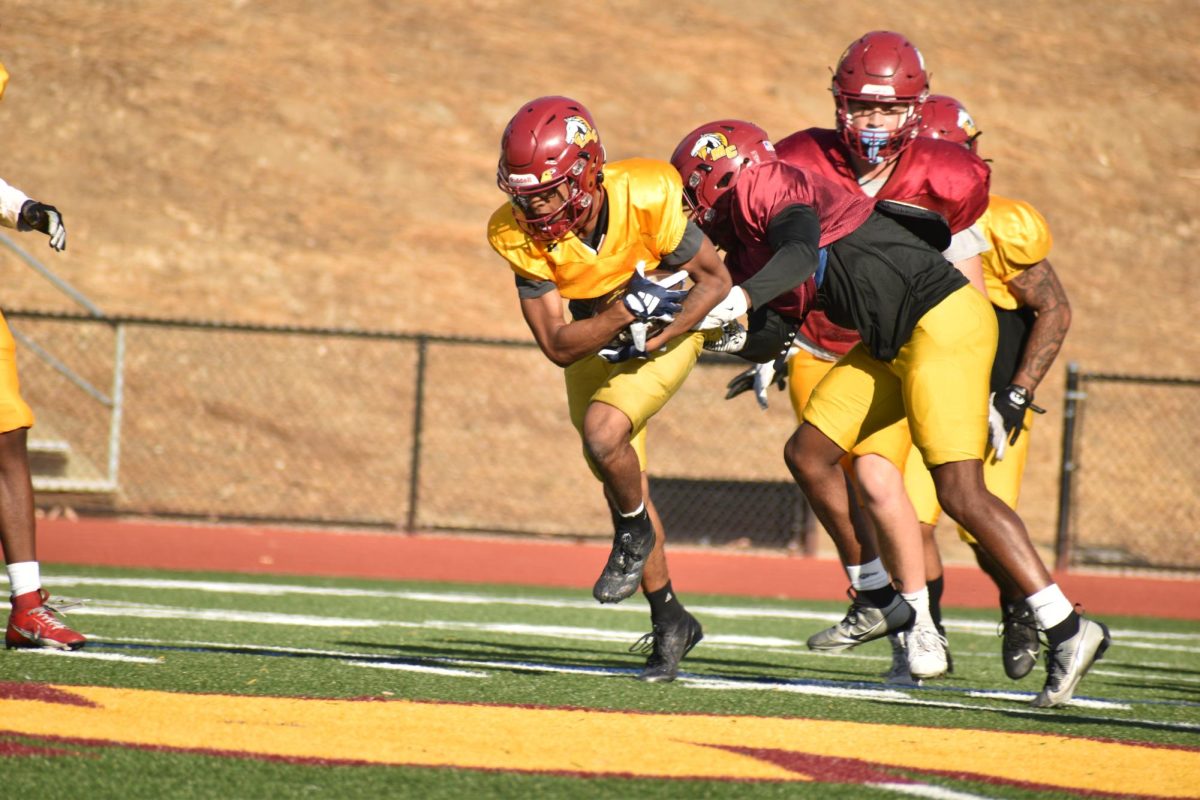 After catching a pass, a Mustangs' receiver holds on to the ball as defenders try to strip it away.