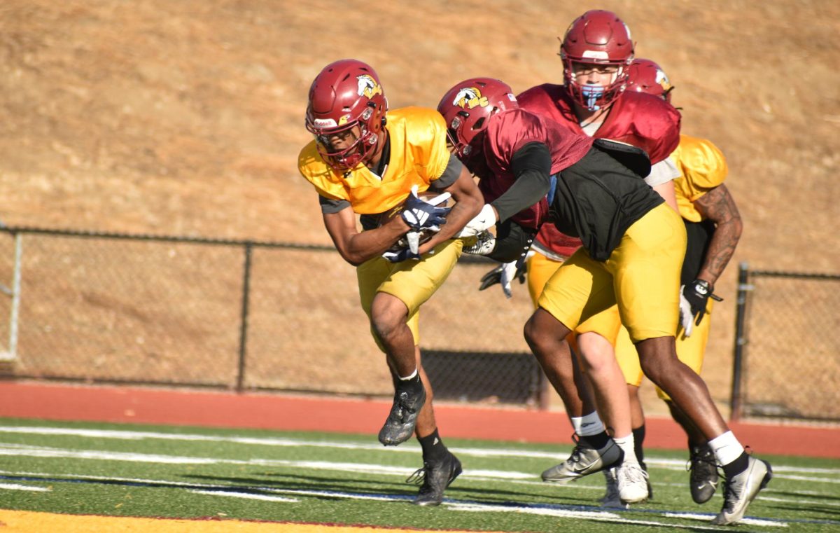 After catching a pass, a Mustangs' receiver holds on to the ball as defenders try to strip it away.