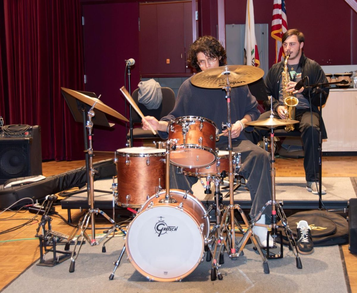 Student Julio Romo plays drums and student plays saxophone while rehearsing.