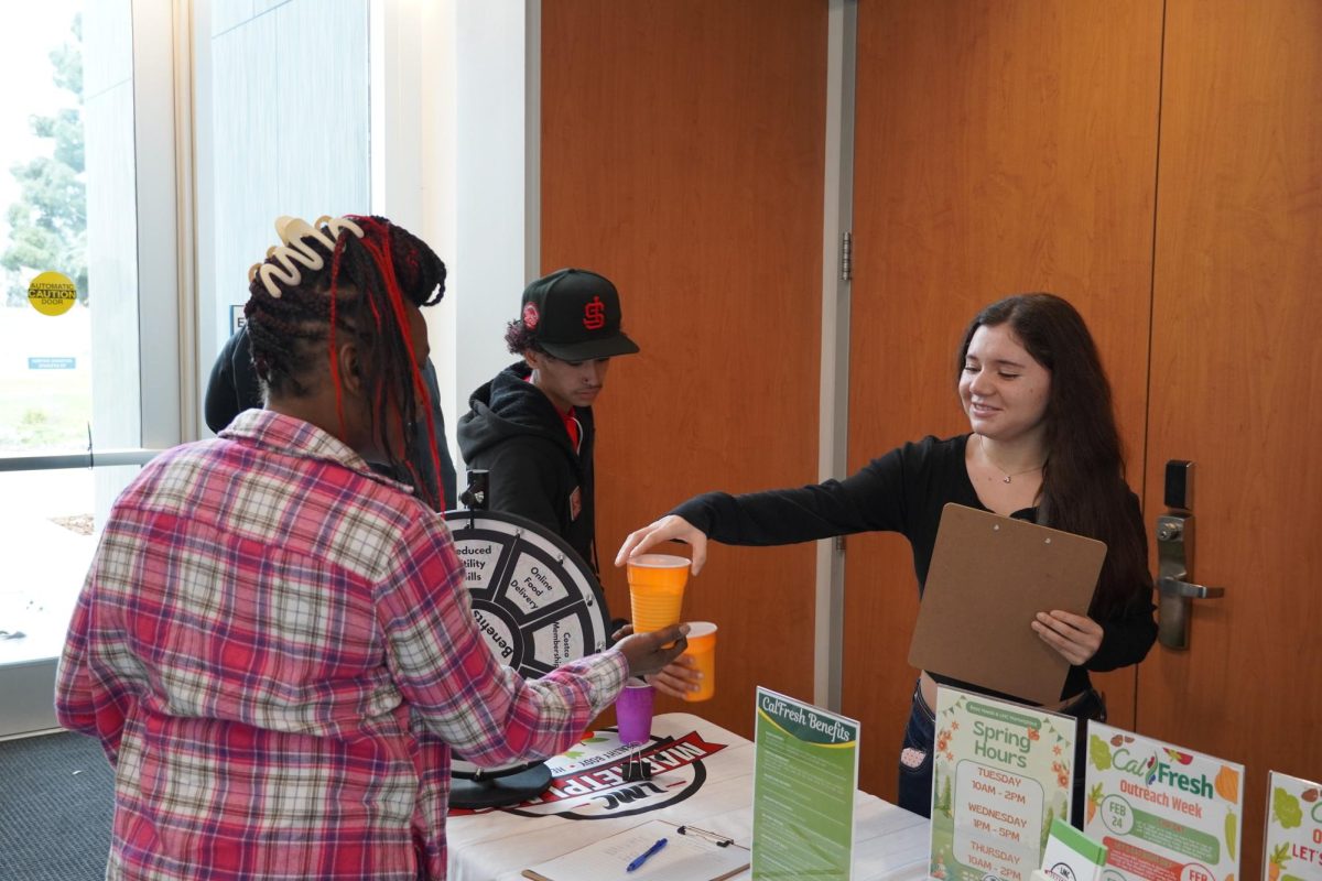 Student worker América Meza Gomez hands a smoothie to student Yamaha Martin during the CalFresh event.