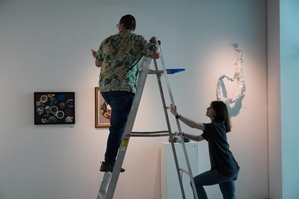 Student worker Jordan Castro examines the gallery from a ladder while Dasha Shevchenko assists him.